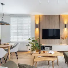 Przytulny salon inspiracje: drewniana ściana z TV, okrągły stół z krzesłami, rośliny i stylowe oświetlenie tworzą ciepłą atmosferę.