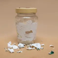 Szklana butelka z resztkami etykiety i oderwanymi fragmentami papieru na powierzchni.