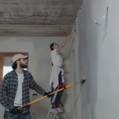 Para malować ściany, mężczyzna i kobieta pracują razem. Ona stoi na drabinie, on trzyma wałek.