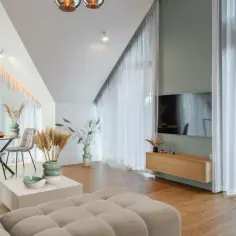 Przytulny salon z sofą w kolorze kremowym, stołem i telewizorem. Jasne zasłony dodają lekkości.