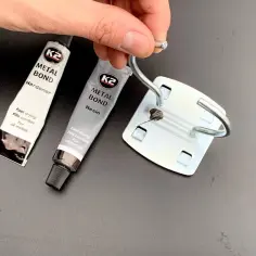 Dwie tubki kleju K2 Metal Bond (utwardzacz i żywica) oraz metalowy element z zaczepem.