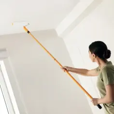 Kobieta z wałkiem maluje sufit. Nowy kolor odświeża wnętrze, a praca idzie sprawnie.